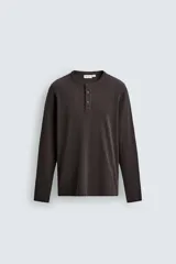Remera de manga larga de corte regular fit, confeccionada en tejido acanalado con mezcla de algodón y efecto lavado. Cuenta con cuello redondo y cierre frontal corto con tres botones.
