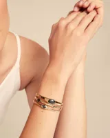 Pulsera rígida dorada de tres vueltas con apliques de cristales negros ovalados.