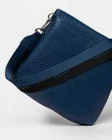 Bandolera color beige con correa ancha de tela negra con el nombre de la marca en blanco.