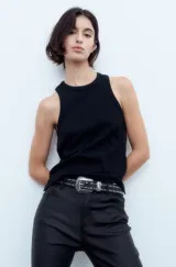 Pantalón jean negro engomado, corte slim, con tajo en el ruedo y cintura con cinturón de cuero con tachas.