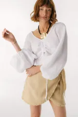 Top de lino italiano color blanco, con escote en V, mangas largas estilo globo y detalle de jareta frontal ajustable con volado en el ruedo.