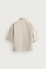 Camisa marrón de corte boxy fit, con tejido estructurado, cuello bowling, manga corta y un bolsillo aplicado en el pecho. Cuenta con cierre frontal de botones.