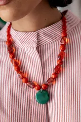 Collar corto compuesto por cuentas de cristal checo en tonos rojos de diversas formas y tamaños, con un medallón central circular de cristal checo en color verde. Incluye cadena de ajuste para regular el largo.