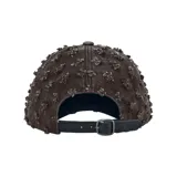 Gorra de denim negro con detalles desgastados y aplicaciones de pedrería dispersas por toda la superficie, con visera curva y el logotipo bordado en la parte frontal.