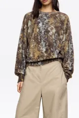 Jersey de punto con textura suave, cuello redondo y mangas largas con puños ajustados. Presenta un diseño de estampado animal print en tonos marrones, grises y azulados.