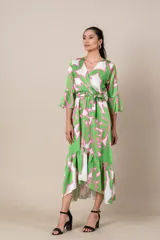 Vestido midi cruzado de satén estampado en tonos verde, blanco y rosa. Tiene lazo en la cintura, mangas 3/4 acampanadas y falda irregular con volados.