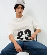 Remera de corte oversized confeccionada en tejido jacquard de color blanco con textura calada. Presenta mangas cortas, cuello redondo y un diseño gráfico deportivo con el número 23 en color negro en la parte frontal.