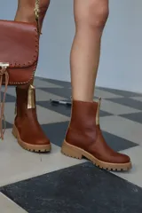 Botas cortas de cuero color marrón con cierre dorado en el frente y suela track color beige.