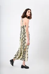 Vestido midi con estampado de piel de serpiente en tonos beige, negro y amarillo. Tiene breteles finos cruzados en la espalda y corte recto.