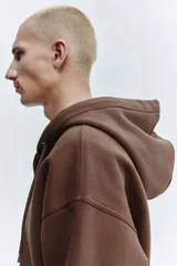 Campera con capucha H&M de corte oversized, confeccionada en tejido pesado de mezcla de algodón con interior cepillado. Presenta cierre frontal, hombros caídos, capucha forrada con cordón de ajuste y bolsillos tipo canguro. Puños y bajo acanalados.