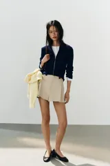 Short de tiro alto color marrón, con pliegues frontales y detalle de botones decorativos en la cintura. Cuenta con bolsillos laterales y cierre frontal con cremallera y gancho metálico.