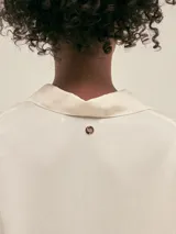 Camisa larga color crema confeccionada en lino-tencel con botones de conchas naturales y bolsillos laterales.