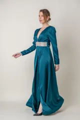 Vestido largo de fiesta en satén de seda color petróleo, con escote en V profundo, mangas largas y falda cruzada con abertura. Presenta aplique de strass en la cintura.