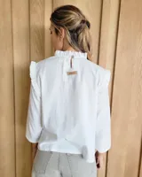 Blusa blanca de manga larga con cuello alto y volados en cuello y hombros.