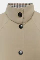 Trench de corte oversize color beige, con cuello alto, cierre frontal de botones y mangas largas con puños vueltos estampados a cuadros. Cuenta con bolsillos delanteros de vivo.