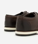 Zapato de vestir acordonado color marrón oscuro, de cuero, con suela blanca y detalles de costuras.