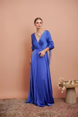 Vestido largo de satén color azul, con escote en V cruzado, mangas tres cuartos con detalles de lazos en los puños y falda larga con tajo frontal.