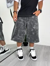 Pantalón de mezclilla gris oscuro con efecto lavado y estampado sutil de hojas o ramas en tono más claro. Diseño de corte muy ancho (baggy) que se puede convertir en short a la altura de la rodilla mediante cierres.