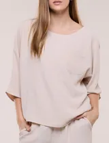 Blusa oversize color negro con caída fluida, escote redondo, bolsillo frontal en el pecho, mangas tres cuartos de hombro caído y costuras a la vista en contraste.