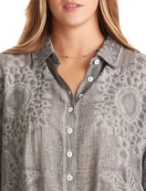 Camisa de algodón color gris con bordados florales en el frente y las mangas. Tiene cuello con solapa y cierre frontal con botones.