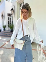 Cartera tipo sobre color crudo, confeccionada en cuero, con correa larga de cuero marrón y costuras decorativas en contraste.