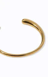 Pulsera rígida de metal dorado con diseño circular abierto y acabado pulido. Presenta una estructura lisa con extremos redondeados y ligeramente cónicos.