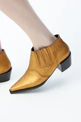 Botines dorados de cuero con punta fina, taco cuadrado bajo y laterales elásticos.