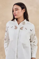 Sobrecamisa blanca de algodón con bordados florales calados en mangas, cuello y pechera. Corte oversize, manga larga y dos bolsillos frontales.