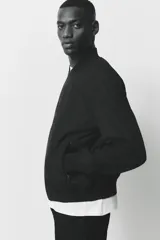 Campera bomber negra, de corte estándar, con cuello elevado acanalado, cierre frontal y bolsillos laterales con cierre. Presenta puños y bajo con ribete acanalado ancho.