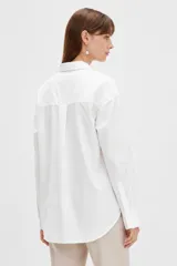 Camisa blanca de algodón, de corte holgado y largo tipo túnica, con cuello camisero, cierre frontal con botones y un bolsillo aplicado en el pecho.