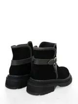 Botín de cuero negro con suela track, detalle de tira con hebilla lateral y costuras a la vista en el borde de la suela.