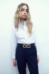 Pantalón de vestir azul marino, de corte slim, con bolsillos laterales y traseros. Se ajusta a la cintura con cinturón de cuero negro con hebilla dorada.