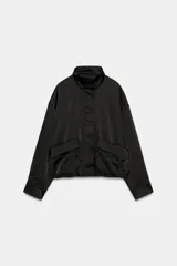 Cazadora satinada de color negro, con cuello subido, manga larga y bolsillos frontales de plastrón con cordones decorativos. Cuenta con bajo elástico y cierre frontal con cremallera y botones a presión oculta.