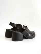 Zapato tipo slingback color negro, con plataforma y taco cuadrado. Presenta una puntera cuadrada y cierre con hebilla metálica en la tira trasera.
