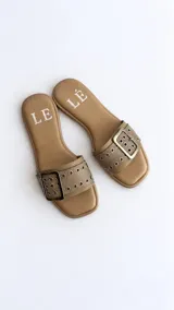 Sandalias planas color tostado, con una tira ancha en el empeine decorada con ojalillos metálicos y una hebilla grande central.