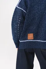 Campera de tejido de punto color marrón con destellos de lurex, corte oversize y cierre frontal. Presenta detalles de costuras y terminaciones en color crema, cuello alto y bolsillos frontales.