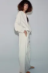 Pantalón de tiro medio color beige, de pierna ancha y corte recto. Cuenta con cintura elástica ajustable con cordones y bolsillos frontales.