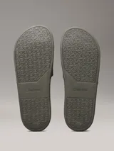 Ojotas tipo slide de color verde oliva, con doble tira superior de TPU con relieve y logotipo grabado. Cuentan con plantilla moldeada ergonómica con soporte para el arco plantar y suela de EVA.
