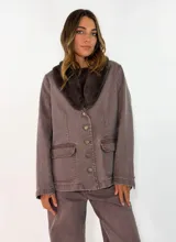 Chaqueta de gabardina color tostado con cuello de piel sintética en tono marrón, cierre frontal con botones y bolsillos delanteros con solapa.