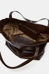 Bolso tipo shopper de gran tamaño, color marrón oscuro, con acabado brillante y doble asa de hombro con pespuntes decorativos. Cuenta con cierre mediante botón imantado y bolsillo interior con cremallera.