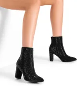 Bota de caña media con tacón cuadrado alto, completamente cubierta de strass negro. Presenta cierre lateral interno y punta ligeramente redondeada.