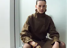 Chaqueta de gabardina color verde militar, de corte oversize con cuello alto abotonado de manera asimétrica, mangas largas con puños ajustables y cinturón ajustable del mismo tejido.