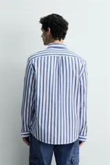 Camisa de corte regular fit confeccionada en tejido de algodón, con diseño de rayas verticales en azul y blanco. Presenta cuello solapa con botones, cierre frontal de botones, manga larga con puños abotonados y un bolsillo en el pecho.