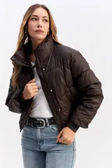 Campera puffer de corte cropped, color marrón oscuro, con cuello alto, cierre frontal con cremallera y botones a presión, y puños elásticos.