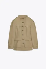 Chaqueta de estilo militar en color beige, con cuello subido, cierre frontal de botones, bolsillos de plastrón con solapa en el delantero y detalle de solapas en el pecho. Presenta mangas largas con hombreras y trabillas decorativas.