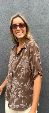 Camisa de corte recto y manga corta con cuello clásico y cierre frontal de botones. Presenta un estampado floral en color blanco sobre una base de color chocolate.