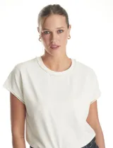 Blusa de crepe color blanco, con cuello redondo y mangas cortas. Presenta apliques de perlas decorativas en el borde del cuello y en los extremos de las mangas.