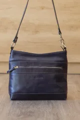 Cartera bandolera Sagali de cuero vacuno en color azul marino, con detalles de cuero grabado en relieve en la banda frontal y la base. Cuenta con un bolsillo frontal con cierre metálico, costuras contrastantes y una correa ajustable.