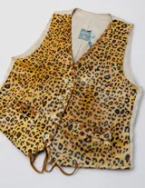 Chaleco sastrero de cuero con estampado animal print, escote en V y bolsillos frontales ribeteados. Presenta detalles de pasamanería en cuero en los bordes y cordones colgantes en el ruedo.