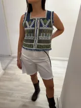 Chaleco corto en denim con bordado artesanal multicolor y escote cuadrado. Con cierre de botones y terminaciones desflecadas.